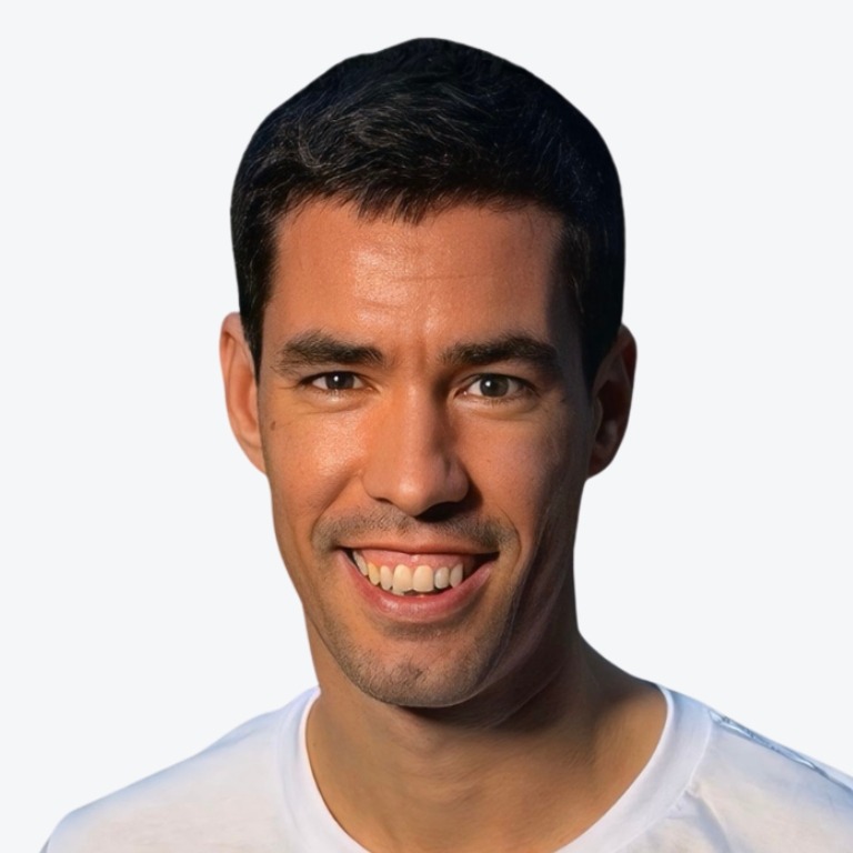 A man with short dark hair and light skin smiles at the camera. He is wearing a plain white t-shirt and posing against a plain, light background.