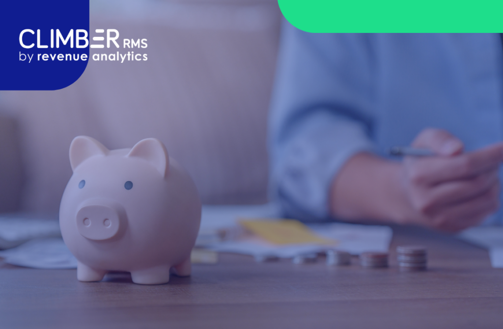 Um cofrinho rosa está sobre uma mesa com moedas e papéis espalhados, enquanto uma pessoa ao fundo segura uma caneta, talvez refletindo sobre o impacto da reforma tributária no setor hoteleiro. O logotipo do Climber RMS, da Revenue Analytics, aparece no canto superior esquerdo.